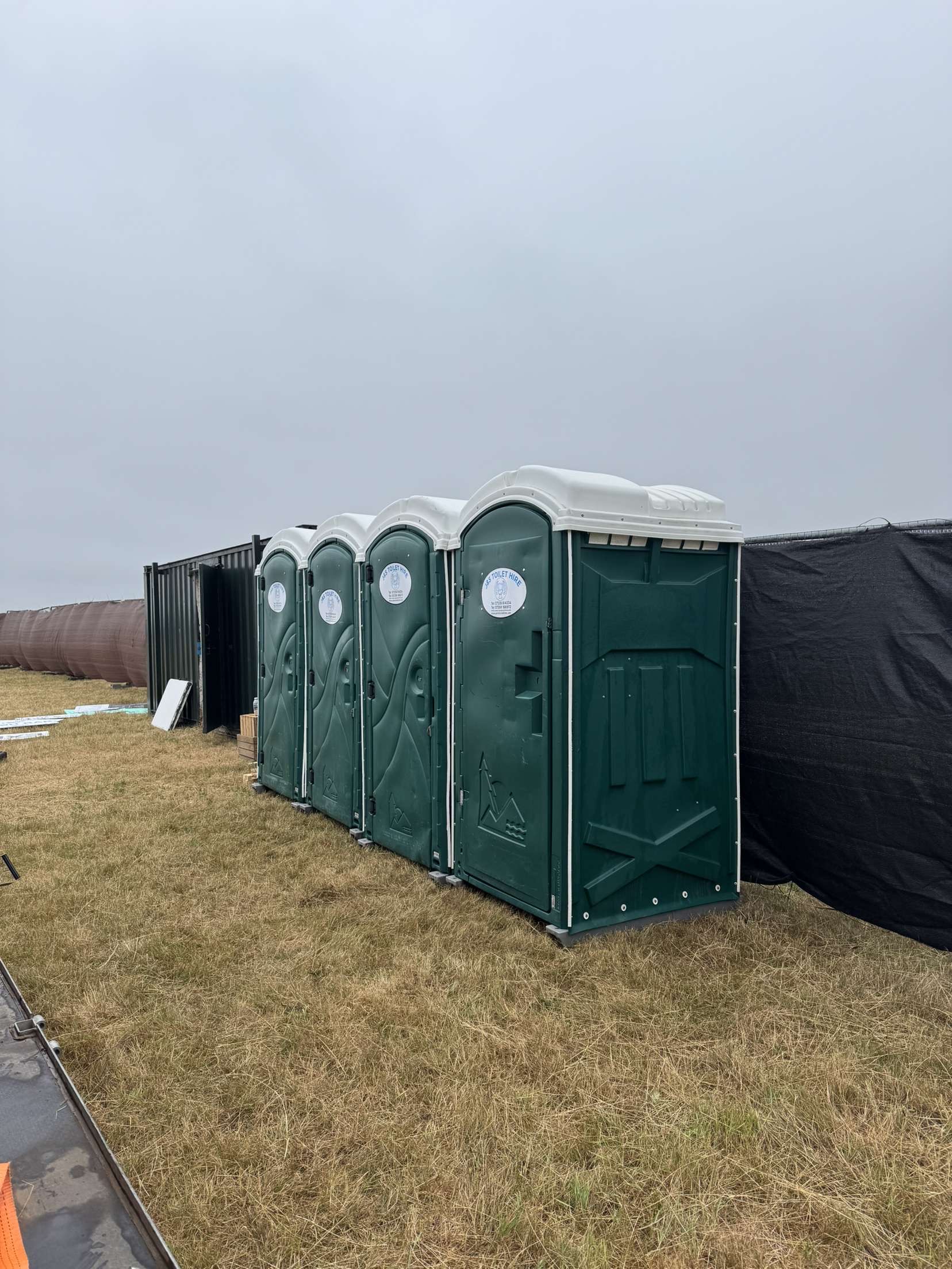 Row of multiple green portable toilets lined up on grass at construction site